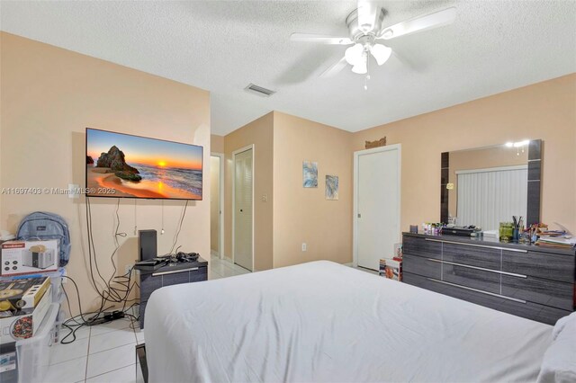 bedroom featuring ceiling fan, light tile patterned floors, and a textured ceiling