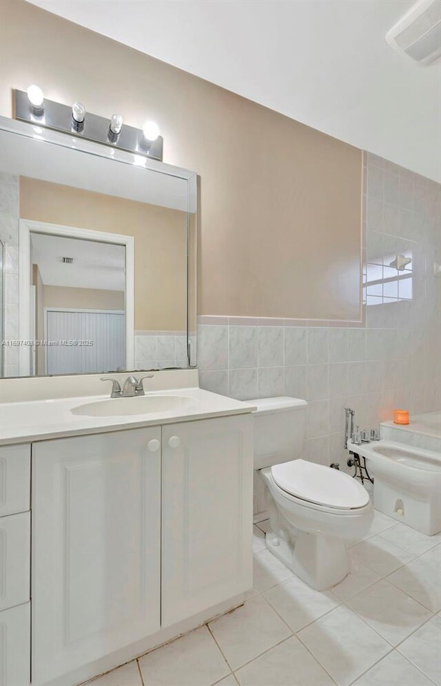 bathroom featuring tile patterned floors, a bidet, toilet, vanity, and tile walls