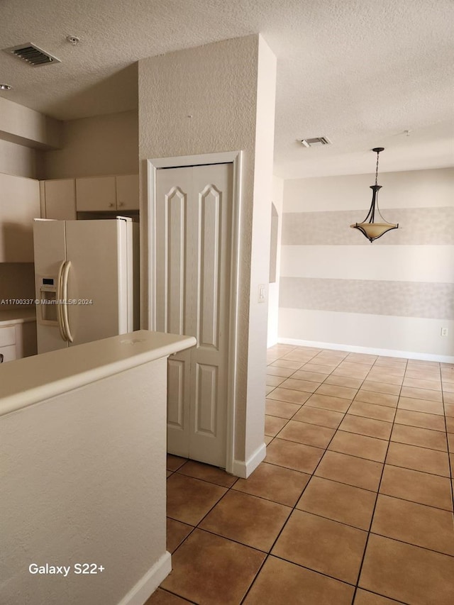 kitchen with a textured ceiling, white fridge with ice dispenser, hanging light fixtures, and light tile patterned floors