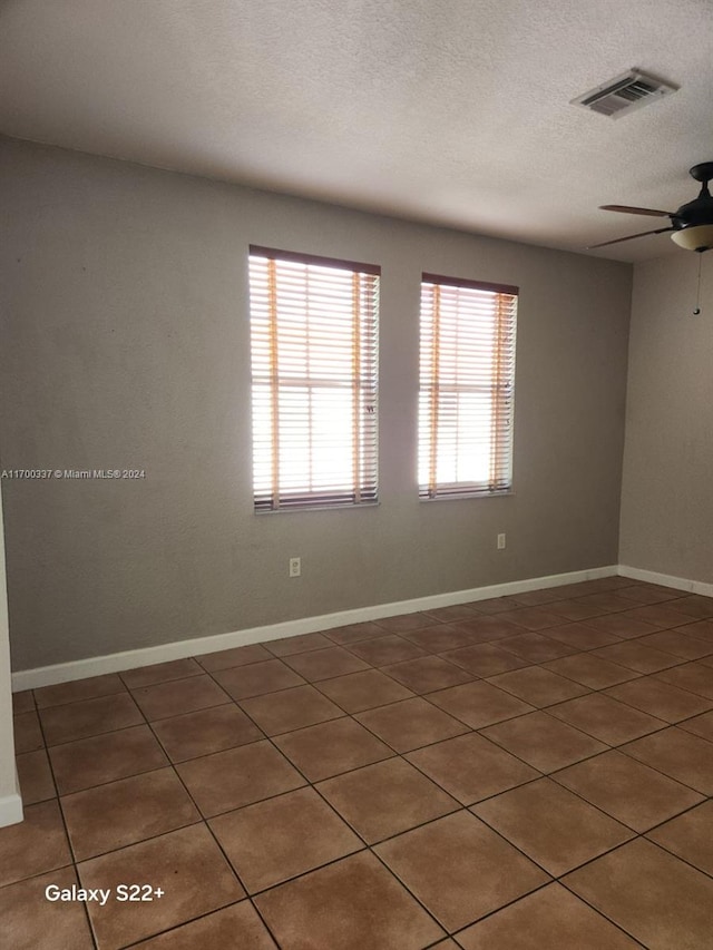 tiled empty room featuring ceiling fan and a textured ceiling