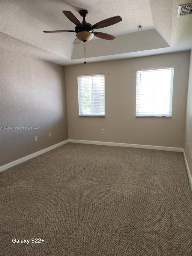 empty room featuring a raised ceiling, ceiling fan, carpet floors, and a textured ceiling