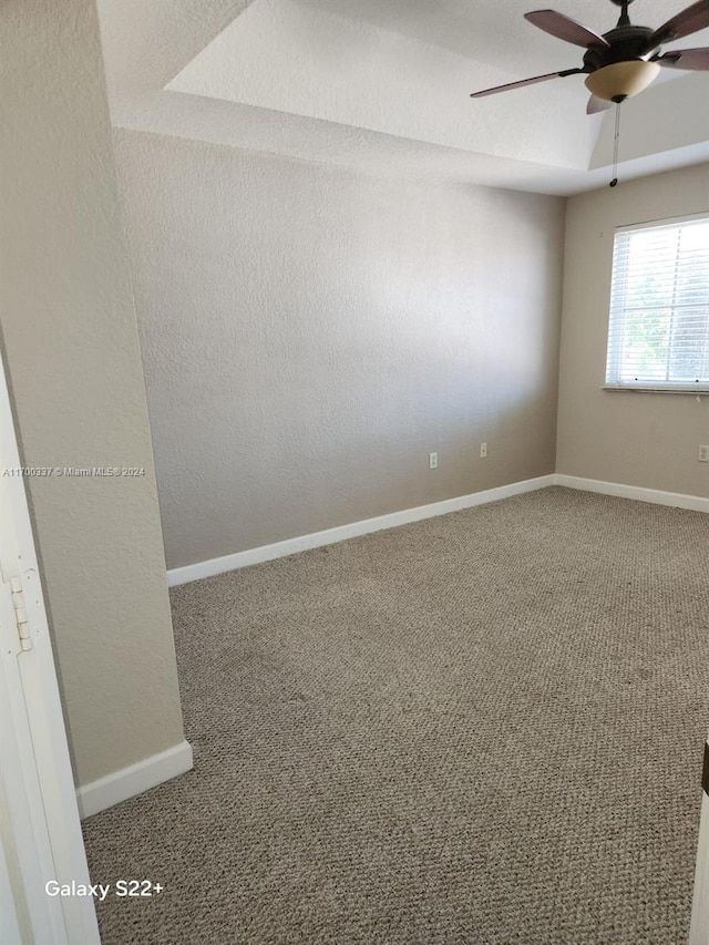 carpeted spare room featuring ceiling fan and a raised ceiling