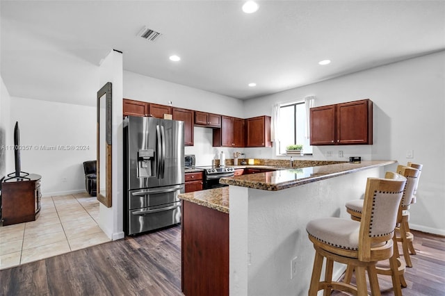 kitchen with kitchen peninsula, a kitchen bar, dark stone counters, stainless steel appliances, and hardwood / wood-style floors