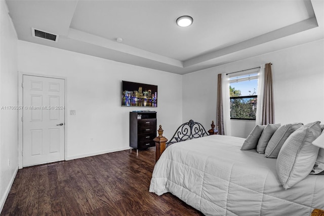 bedroom featuring a raised ceiling and dark wood-type flooring