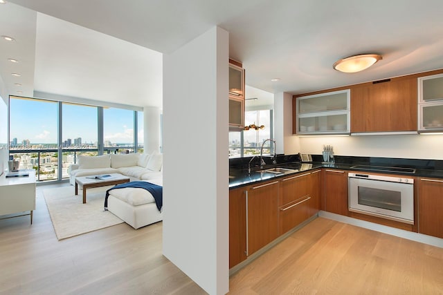 kitchen with floor to ceiling windows, sink, stovetop, oven, and light hardwood / wood-style floors