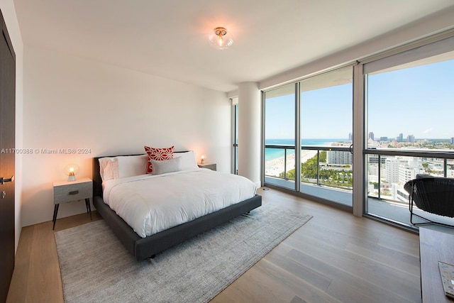 bedroom featuring access to outside, a water view, expansive windows, and hardwood / wood-style floors