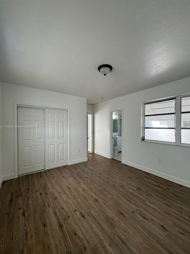 unfurnished bedroom featuring a closet, ensuite bathroom, and dark hardwood / wood-style flooring