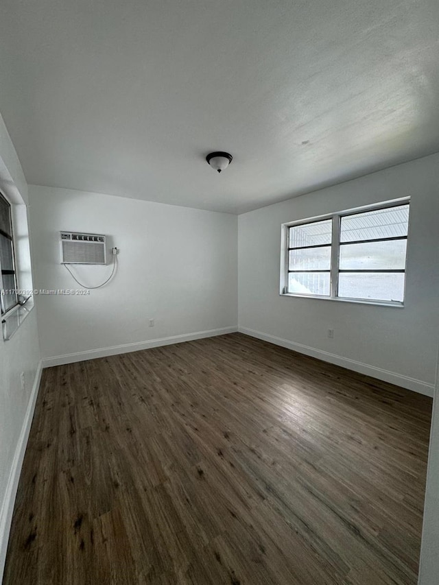 empty room with an AC wall unit and dark hardwood / wood-style floors