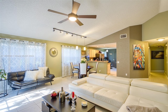 living room with a textured ceiling, ceiling fan, light tile patterned flooring, and vaulted ceiling