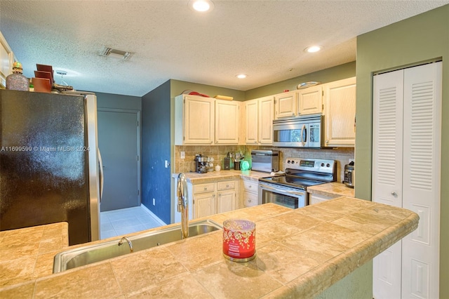 kitchen with tile countertops, a textured ceiling, backsplash, and stainless steel appliances