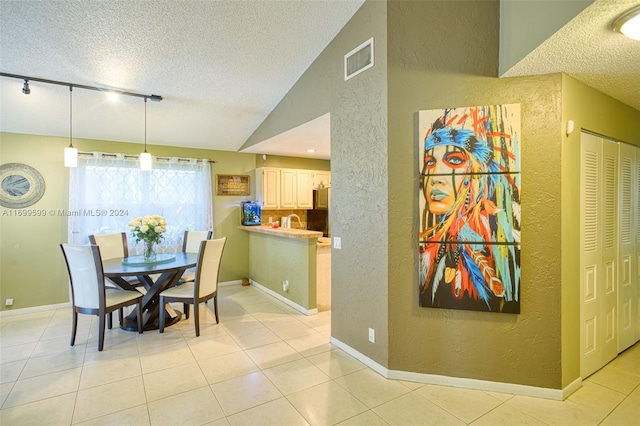 dining space featuring sink, lofted ceiling, track lighting, a textured ceiling, and light tile patterned flooring