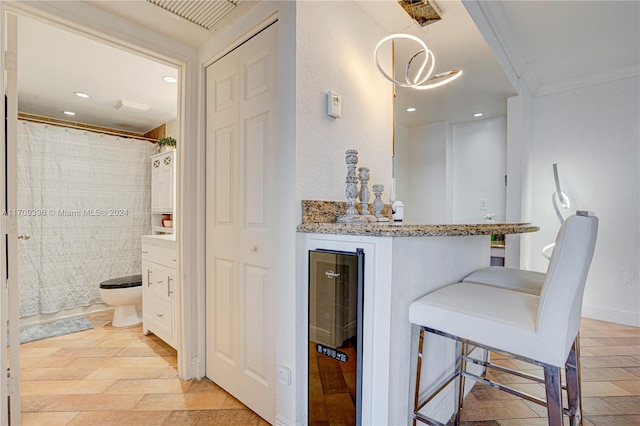 bar with light stone countertops, ornamental molding, decorative light fixtures, white cabinets, and wine cooler