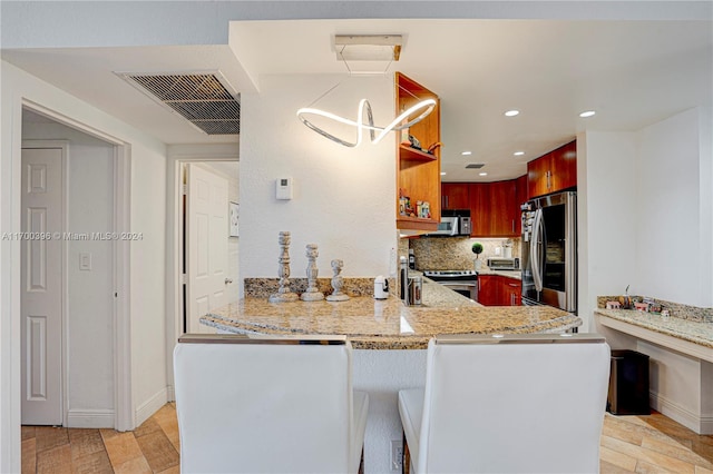 kitchen featuring light stone countertops, backsplash, kitchen peninsula, decorative light fixtures, and appliances with stainless steel finishes