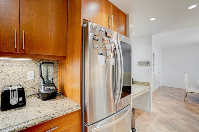 kitchen featuring tasteful backsplash, stainless steel fridge, light stone countertops, and light wood-type flooring