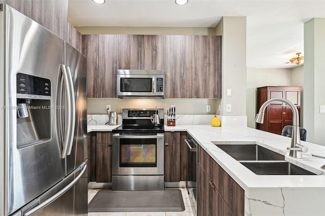 kitchen featuring sink, light tile patterned floors, light stone countertops, appliances with stainless steel finishes, and kitchen peninsula