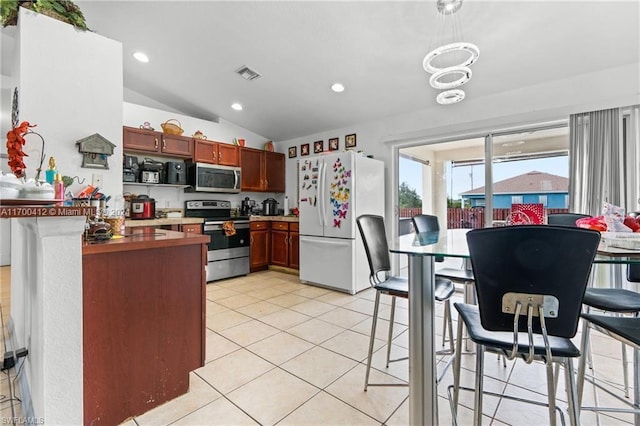 kitchen featuring hanging light fixtures, kitchen peninsula, vaulted ceiling, light tile patterned flooring, and appliances with stainless steel finishes