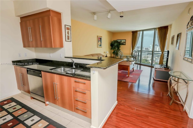 kitchen with kitchen peninsula, stainless steel dishwasher, sink, light hardwood / wood-style flooring, and dark stone countertops