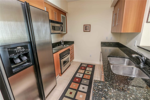 kitchen with dark stone countertops, sink, light tile patterned flooring, and stainless steel appliances