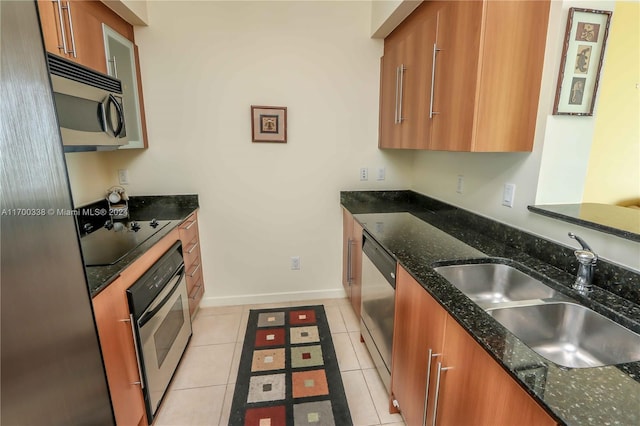 kitchen featuring appliances with stainless steel finishes, light tile patterned floors, dark stone countertops, and sink