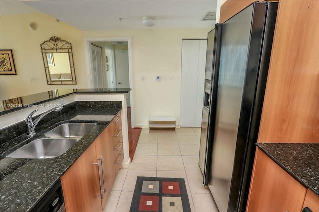 kitchen with dark stone counters, black fridge, sink, dishwashing machine, and light tile patterned flooring