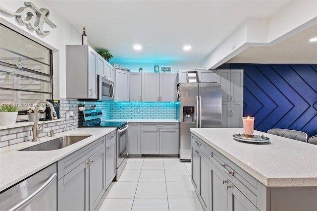 kitchen featuring decorative backsplash, light stone countertops, stainless steel appliances, sink, and light tile patterned floors