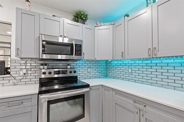 kitchen featuring gray cabinets, light stone counters, appliances with stainless steel finishes, and tasteful backsplash