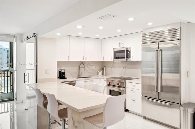 kitchen with kitchen peninsula, a breakfast bar, sink, high quality appliances, and white cabinetry