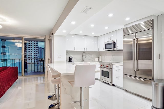 kitchen with tasteful backsplash, a breakfast bar, light tile patterned floors, high quality appliances, and white cabinetry