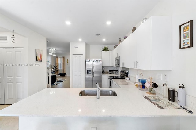 kitchen with sink, kitchen peninsula, stainless steel appliances, light stone countertops, and white cabinets