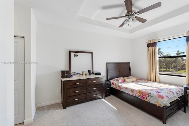 bedroom with ceiling fan, light colored carpet, and a raised ceiling