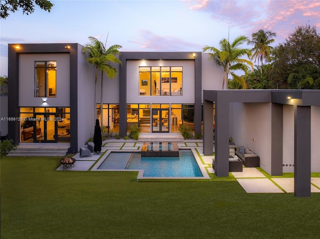 back house at dusk with a lawn, a patio area, french doors, and an outdoor hangout area