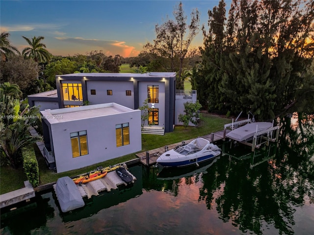 back house at dusk featuring a lawn and a water view