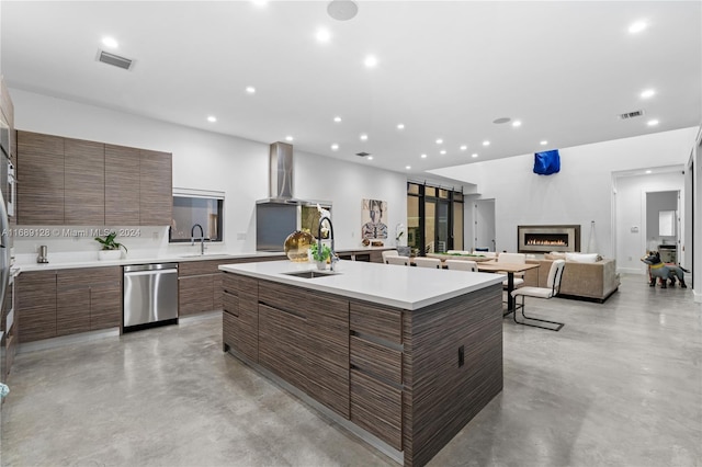 kitchen with sink, stainless steel dishwasher, wall chimney exhaust hood, and an island with sink