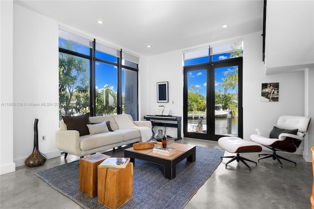 living room with floor to ceiling windows, concrete floors, a water view, and plenty of natural light