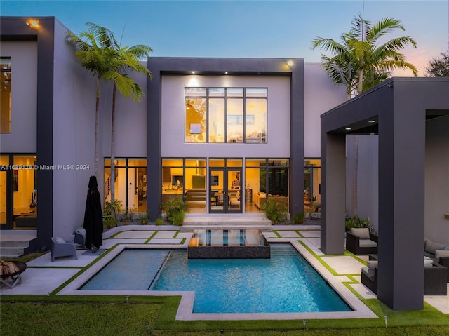 back house at dusk featuring a patio area and a pool with hot tub