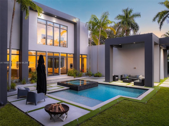 back house at dusk featuring french doors, a patio, an outdoor living space with a fire pit, and a pool with hot tub