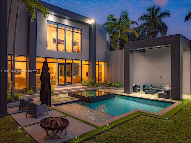 pool at dusk featuring an in ground hot tub, a patio, and an outdoor living space with a fire pit