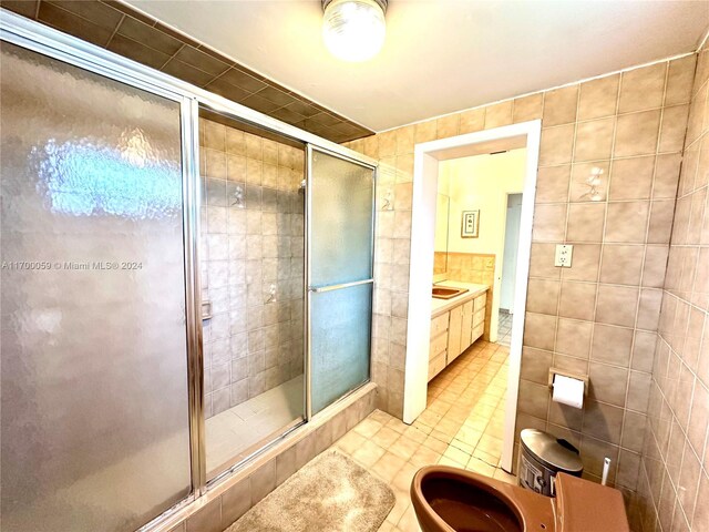 bathroom featuring tile patterned floors, vanity, a shower with shower door, and tile walls