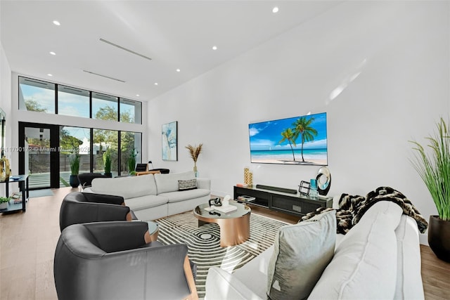 living room with a high ceiling, floor to ceiling windows, french doors, and light hardwood / wood-style flooring