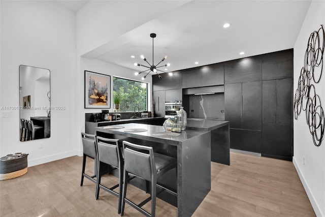 kitchen featuring pendant lighting, sink, a kitchen breakfast bar, a center island, and light hardwood / wood-style flooring