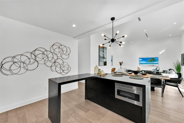 kitchen featuring stainless steel microwave, kitchen peninsula, a chandelier, and light hardwood / wood-style flooring