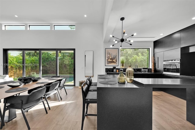 kitchen with a breakfast bar, decorative light fixtures, a notable chandelier, oven, and light hardwood / wood-style floors