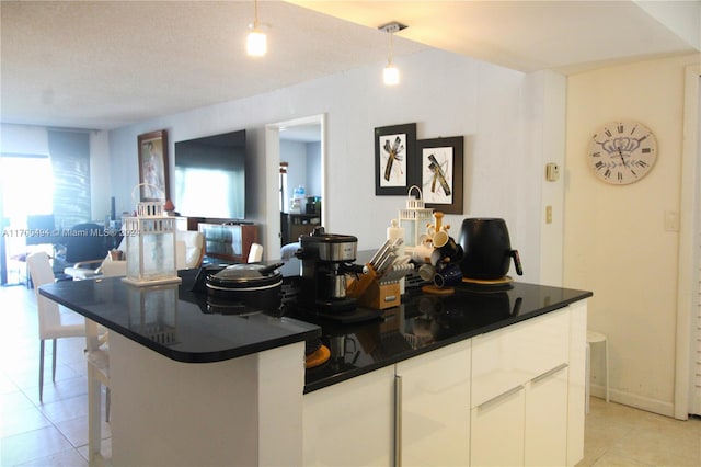 kitchen with a textured ceiling, light tile patterned floors, decorative light fixtures, a center island with sink, and white cabinetry