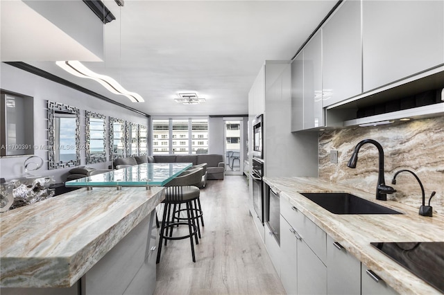 kitchen featuring pendant lighting, white cabinets, sink, light hardwood / wood-style flooring, and a kitchen bar