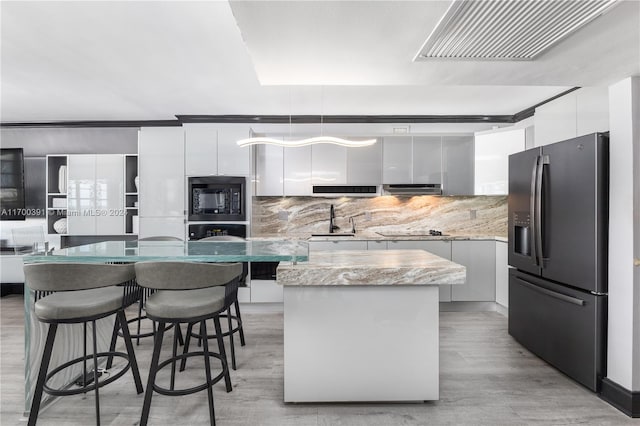 kitchen with white cabinetry, tasteful backsplash, light hardwood / wood-style floors, a kitchen island, and black appliances