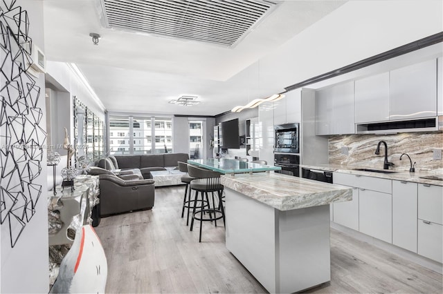 kitchen with a kitchen island, white cabinetry, light hardwood / wood-style floors, oven, and stainless steel microwave