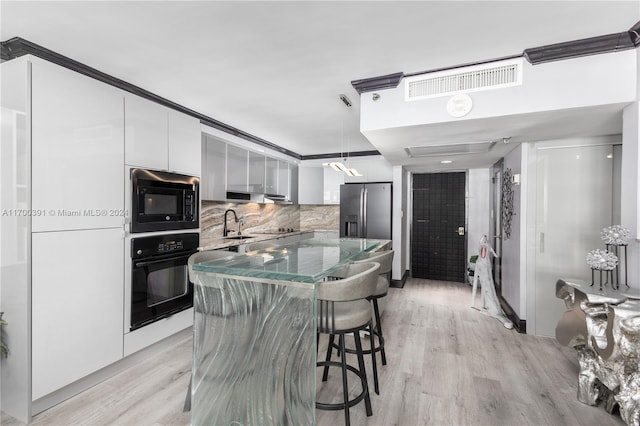 kitchen with backsplash, black appliances, light hardwood / wood-style flooring, white cabinets, and a kitchen island