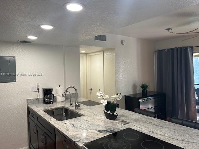 kitchen featuring a textured ceiling, dark brown cabinets, light stone counters, and sink