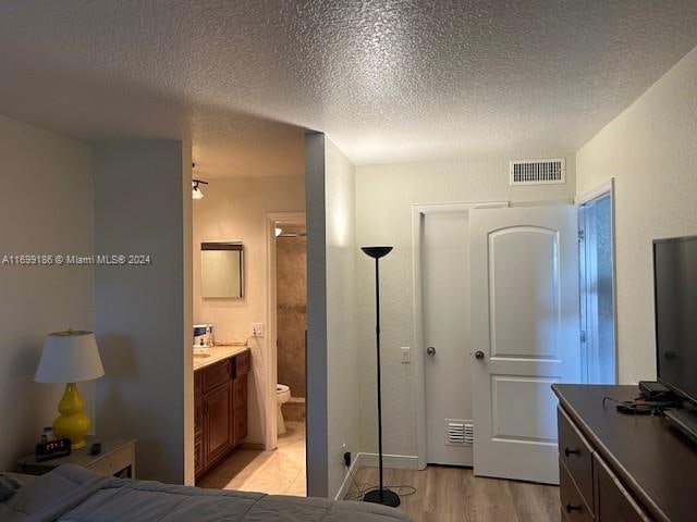 bedroom featuring light wood-type flooring, a textured ceiling, and ensuite bathroom