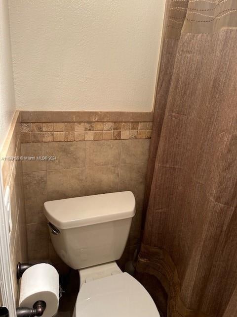 bathroom featuring toilet and tile walls